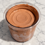 Chocolate Ninja Creami ice cream without protein powder in a pint container on a marble countertop.
