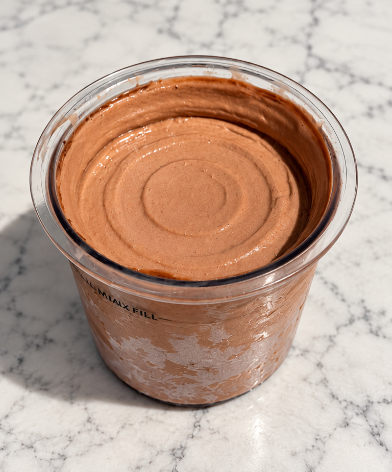 Chocolate Ninja Creami ice cream without protein powder in a pint container on a marble countertop.