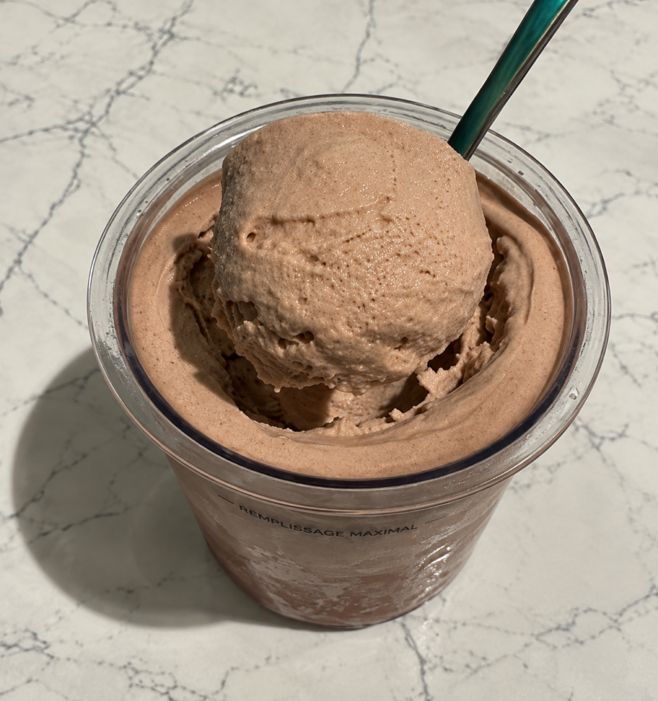 Spoon lifting a scoop of High-Protein Chocolate Ninja Creami above the pint to show its thick and creamy texture.