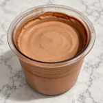 High-Protein Chocolate Pudding Ninja Creami in a clear pint container with a smooth, creamy chocolate surface
