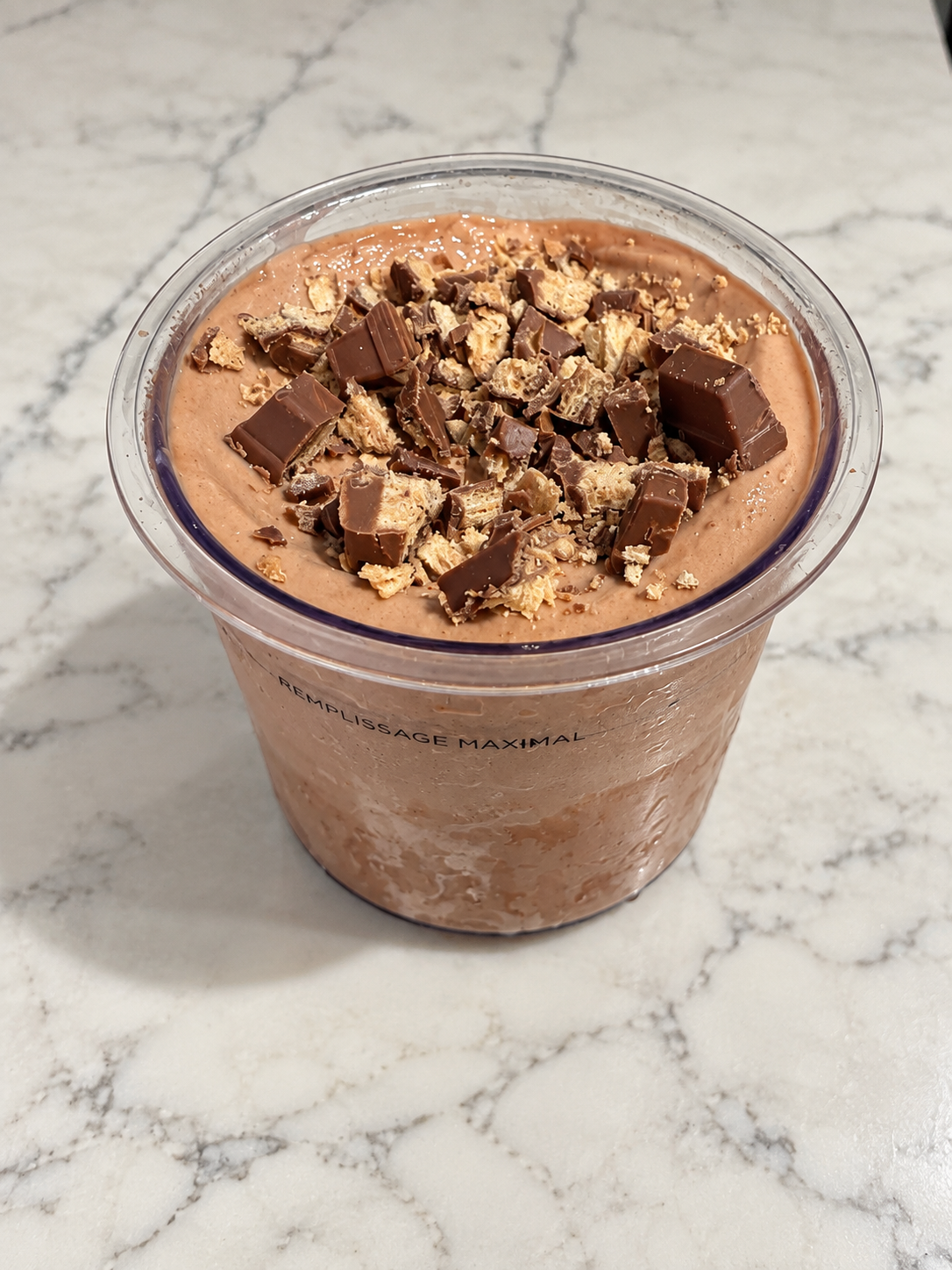 High-Protein Kit Kat Chocolate Ninja Creami topped with chopped Kit Kat pieces in a Ninja Creami pint.