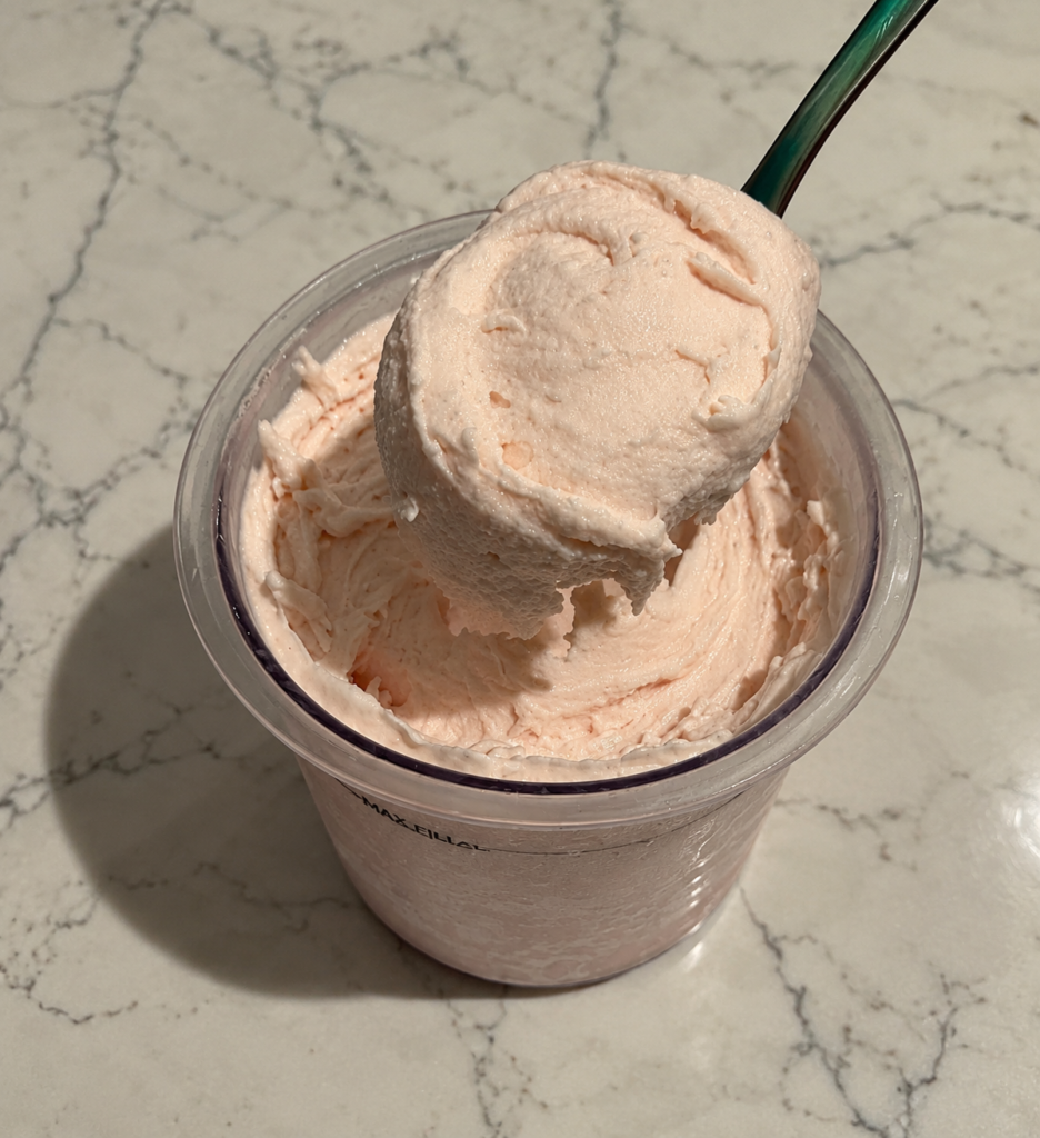 Green spoon lifting a thick scoop of High-Protein Strawberry Ninja Creami above the pint, showing its creamy texture.