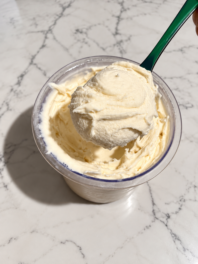 Green spoon lifting a scoop of High-Protein Vanilla Ninja Creami, showing the thick and creamy vanilla ice cream texture.