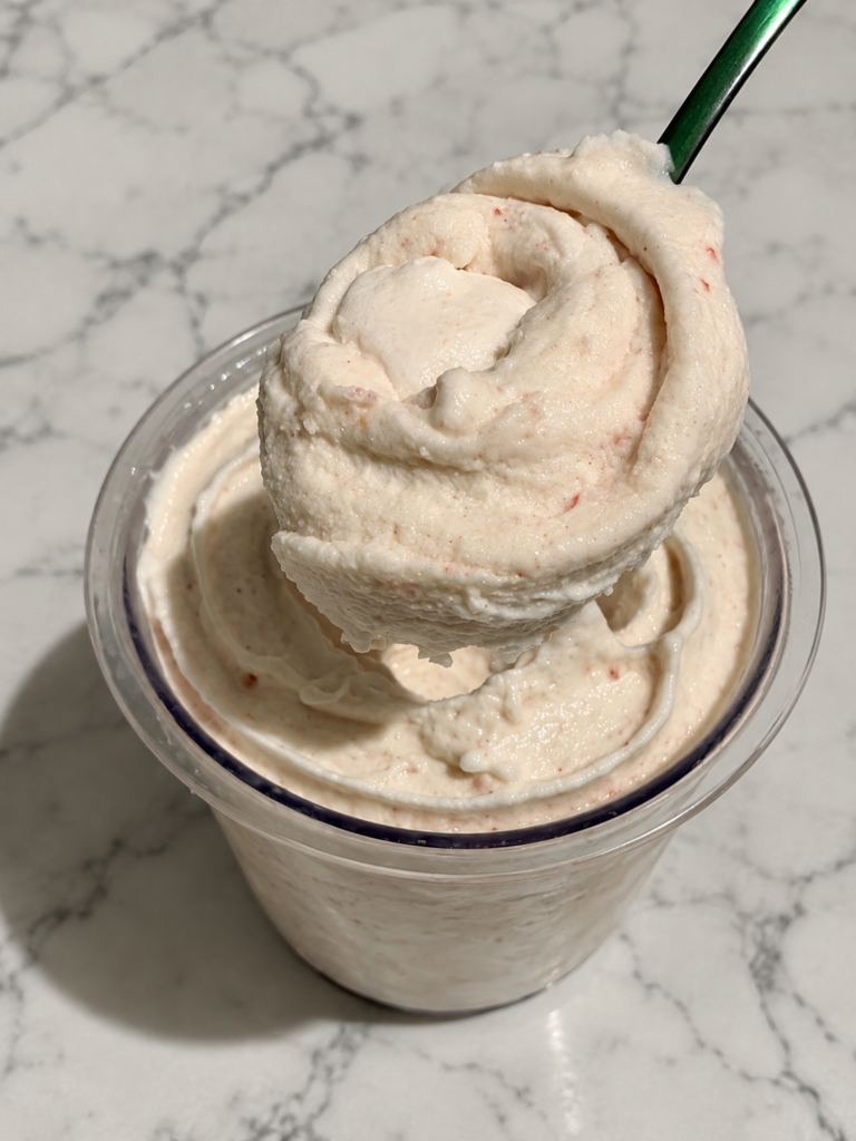 Spoonful of creamy strawberry cheesecake Ninja Creami ice cream lifted above the pint.