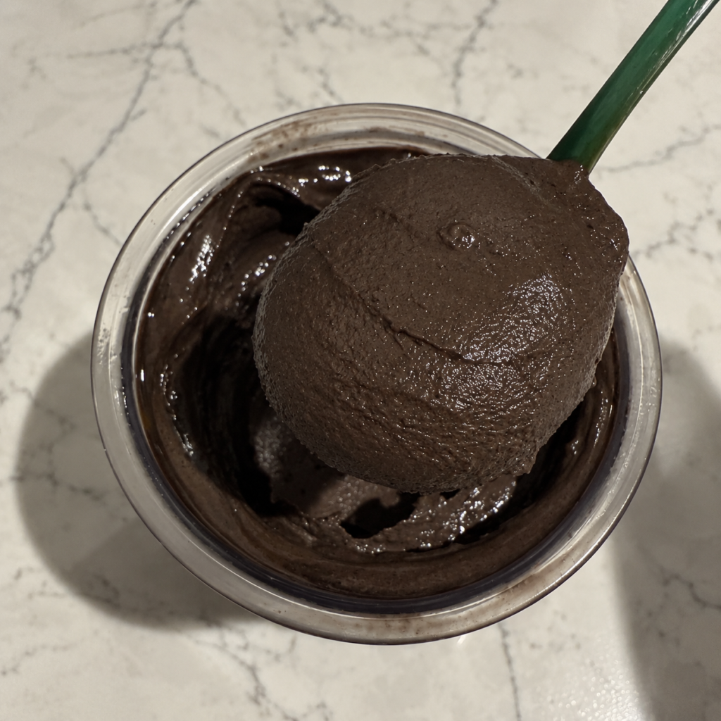 Green spoon lifting a thick scoop of Dark Chocolate Ninja Creami from the pint.